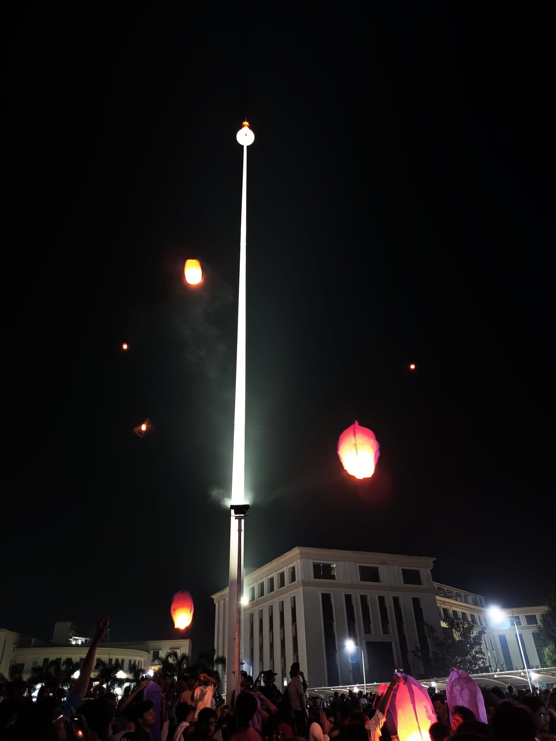 Sky lanterns rising at night beside a tall lit pole