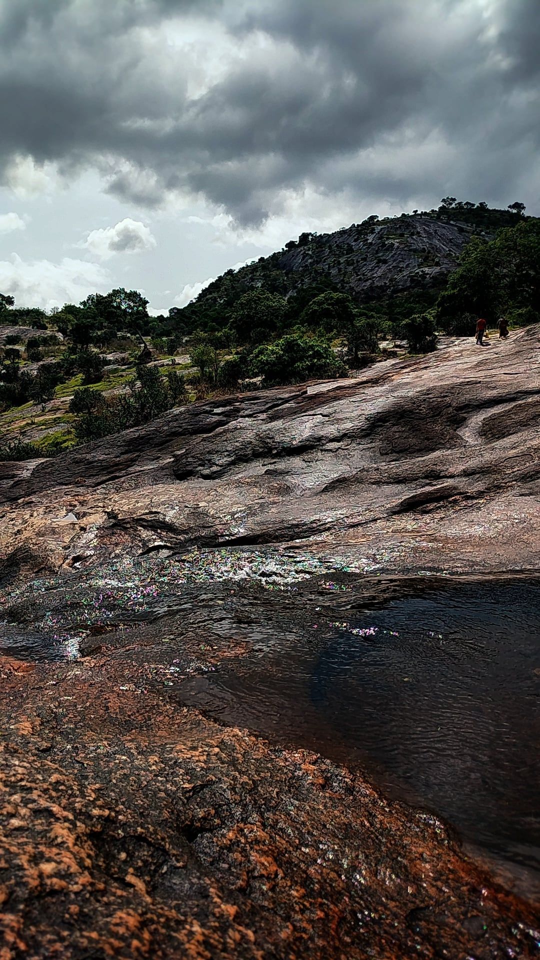 Bare rock rising towards a hill under heavy clouds
